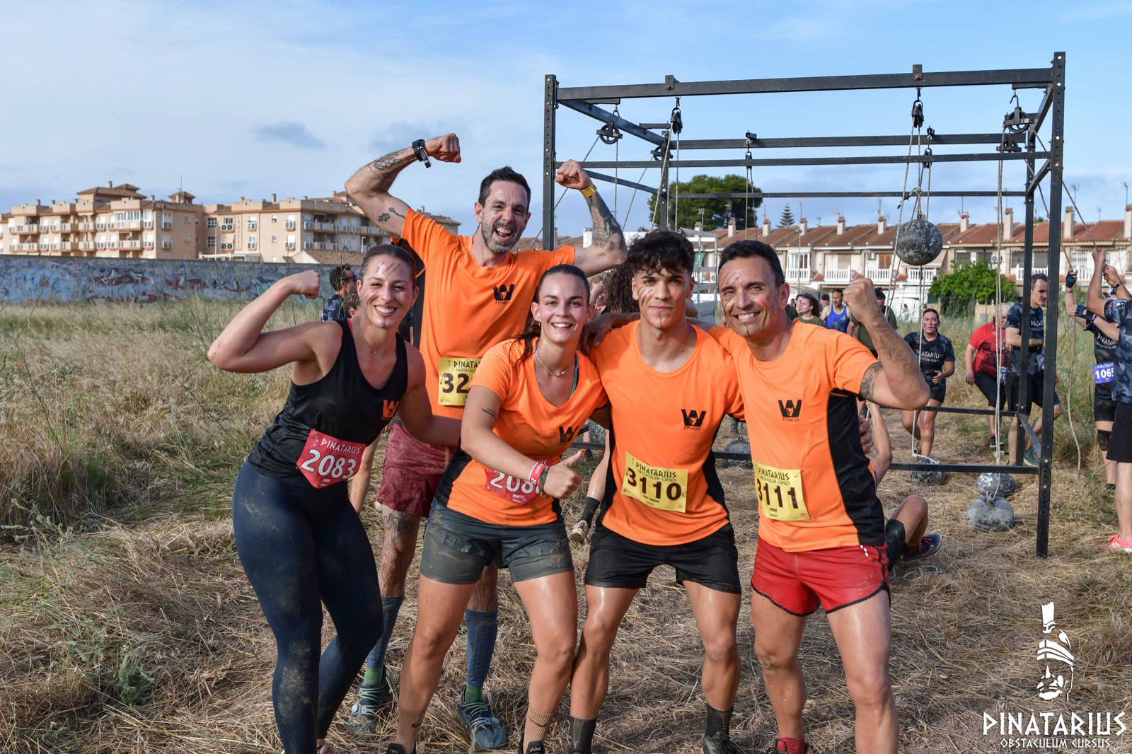 Cinco miembros de Wolf Fitness sacando bíceps junto a un obstáculo de la carrera